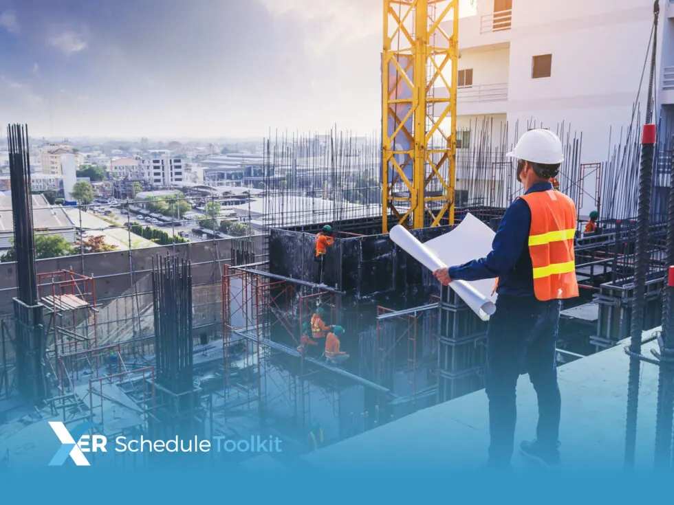 Man in hard hat and hi-vis vest, stood on a construction site holding a large piece of paper, looking into the distance, while other men work on the site